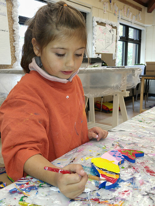 A child uses a paintbrush to decorate their wooden fish.