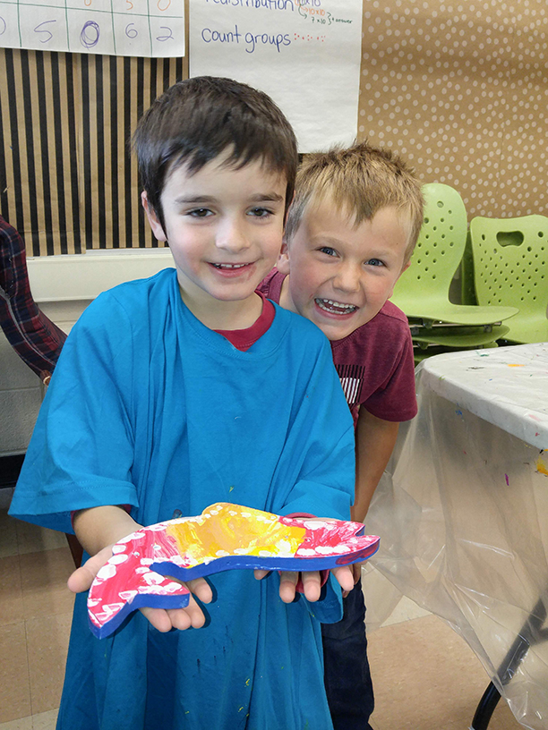 A child holds up their wooden fish with a friend smiling beside them proudly.