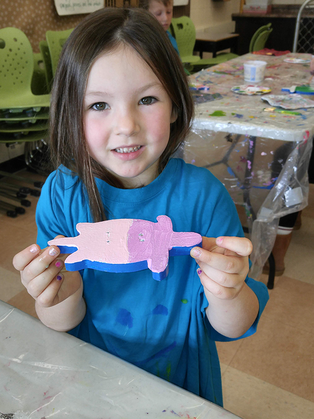 A smiling child holds up their decorated wooden fish from the Stream of Dreams Program..